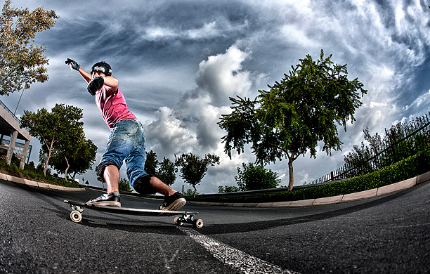 Bottom view of professional skateboarder leaning sideways surrounded by trees and blue skies