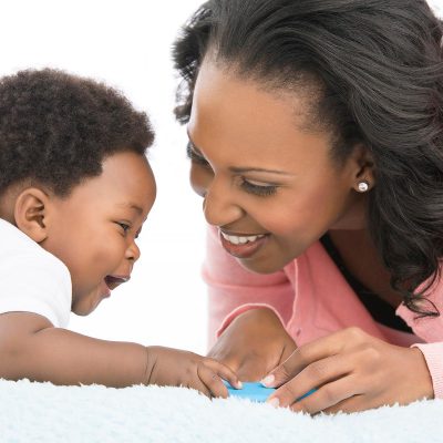 mom and baby interacting with toy on white blanket