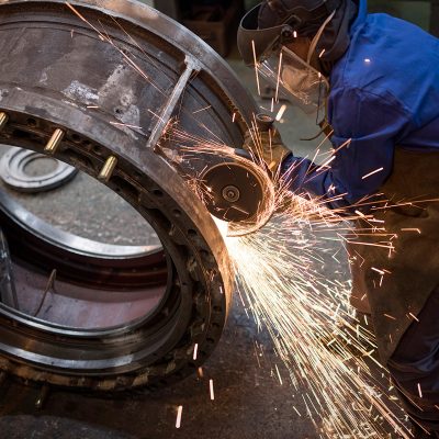Man wearing protective gear welding cylindrical object causing bright sparks